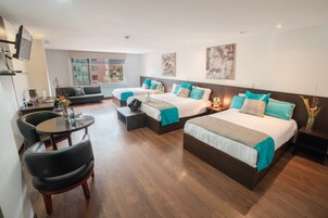 Habitación de hotel con dos camas, un sofá, una mesa de comedor y un televisor.
