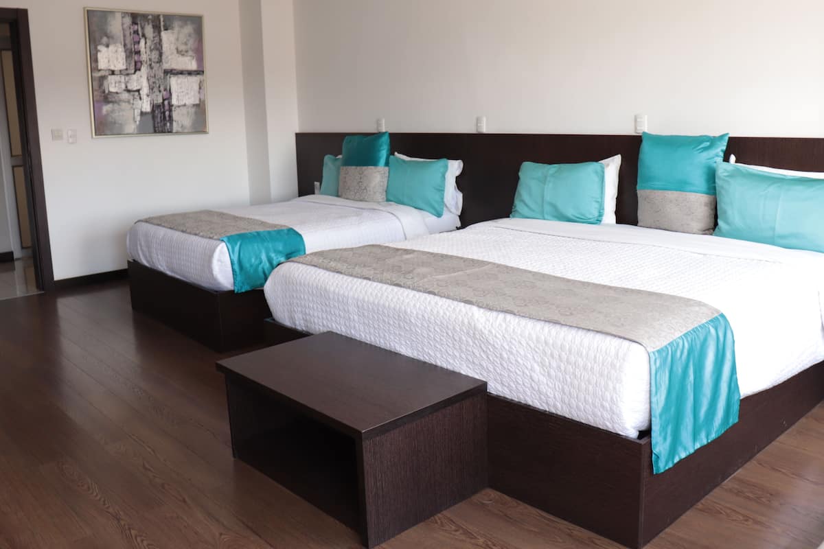 Two plush beds with matching headboards and decorative pillows sit atop white linens in a serene space.