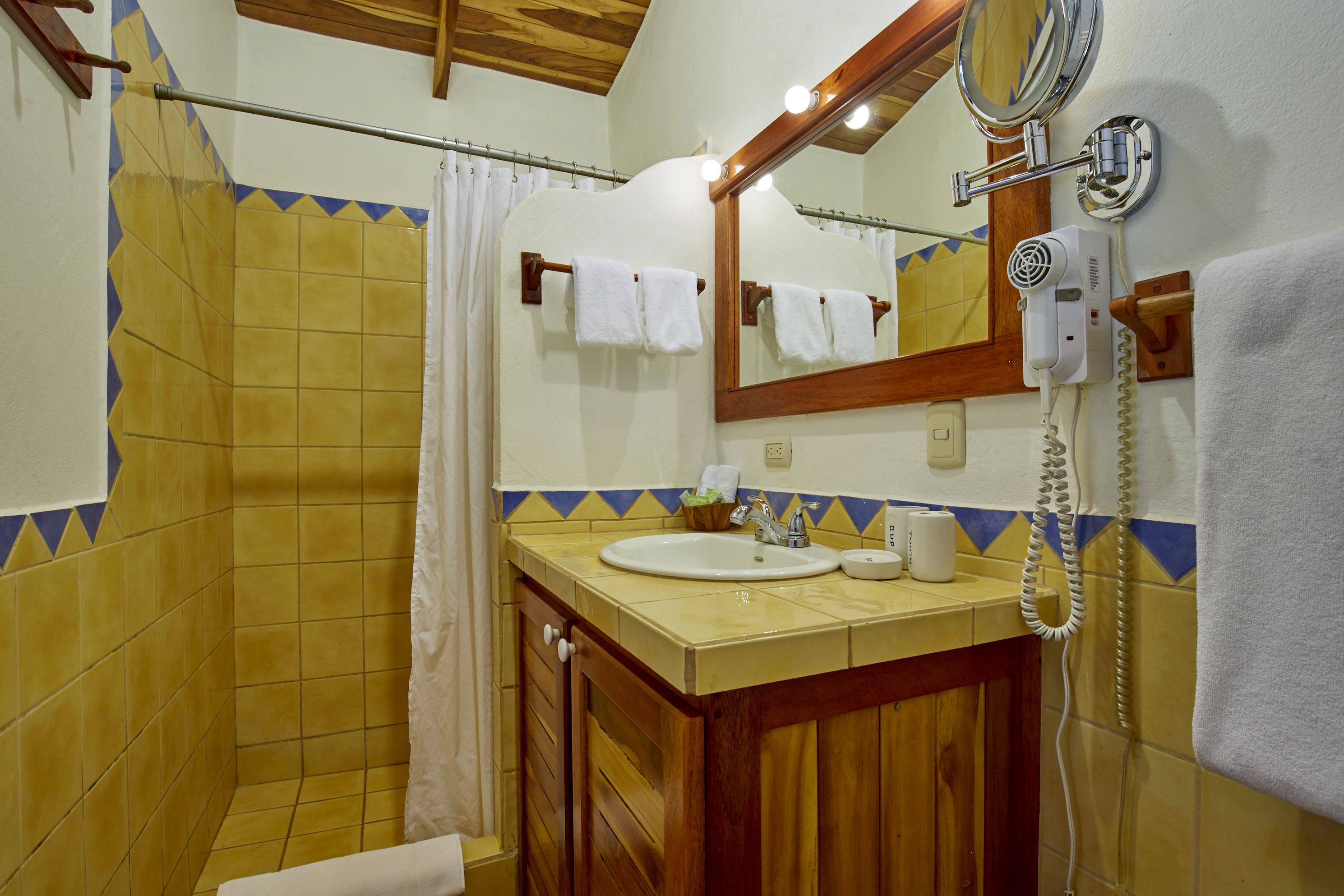 Un baño con tocador de madera, lavamanos, espejo, secador de pelo y cortina de ducha.