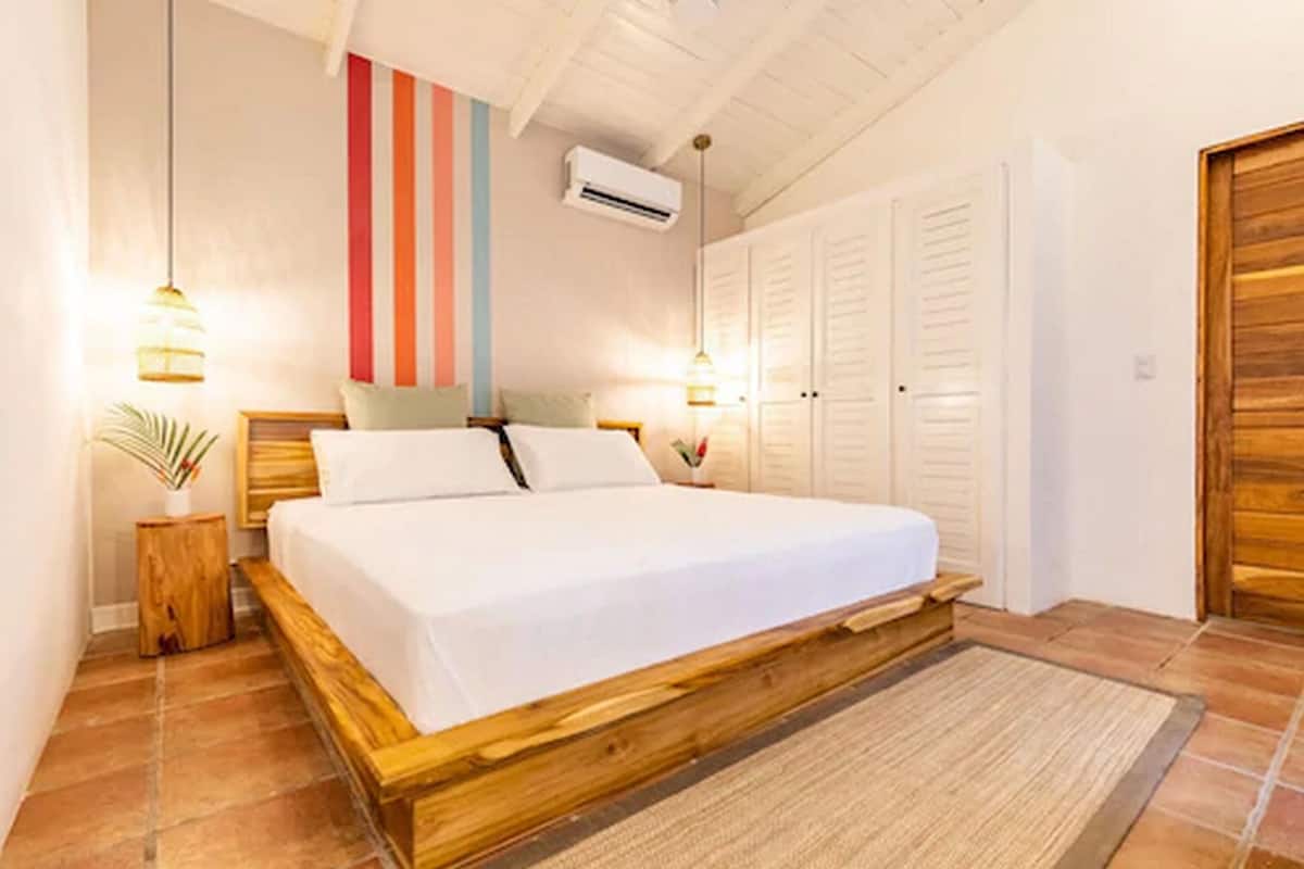 A bedroom with a wooden bed, white bedding, a striped wall, and a wooden door.