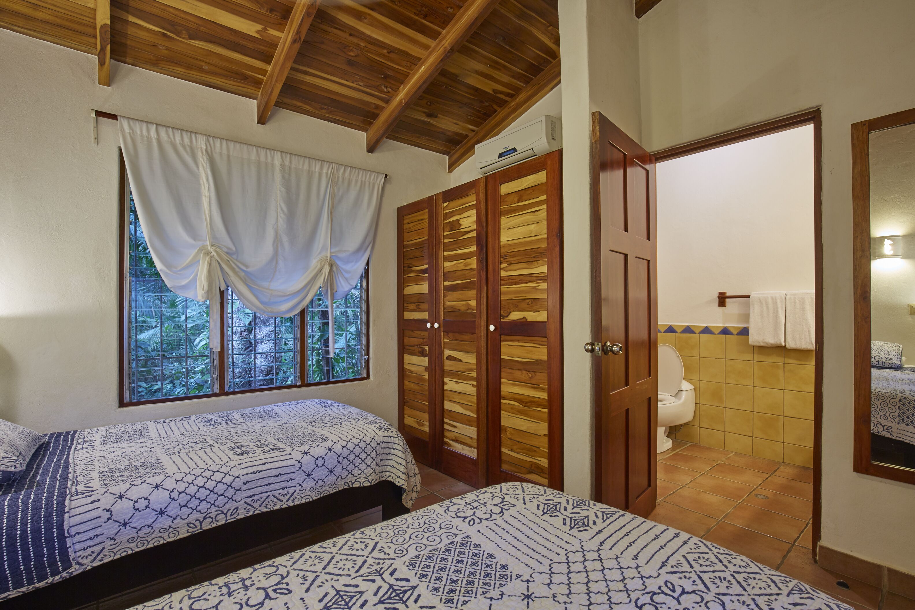 Una camera da letto con due letti, un soffitto in legno, una finestra con tende e un armadio in legno.