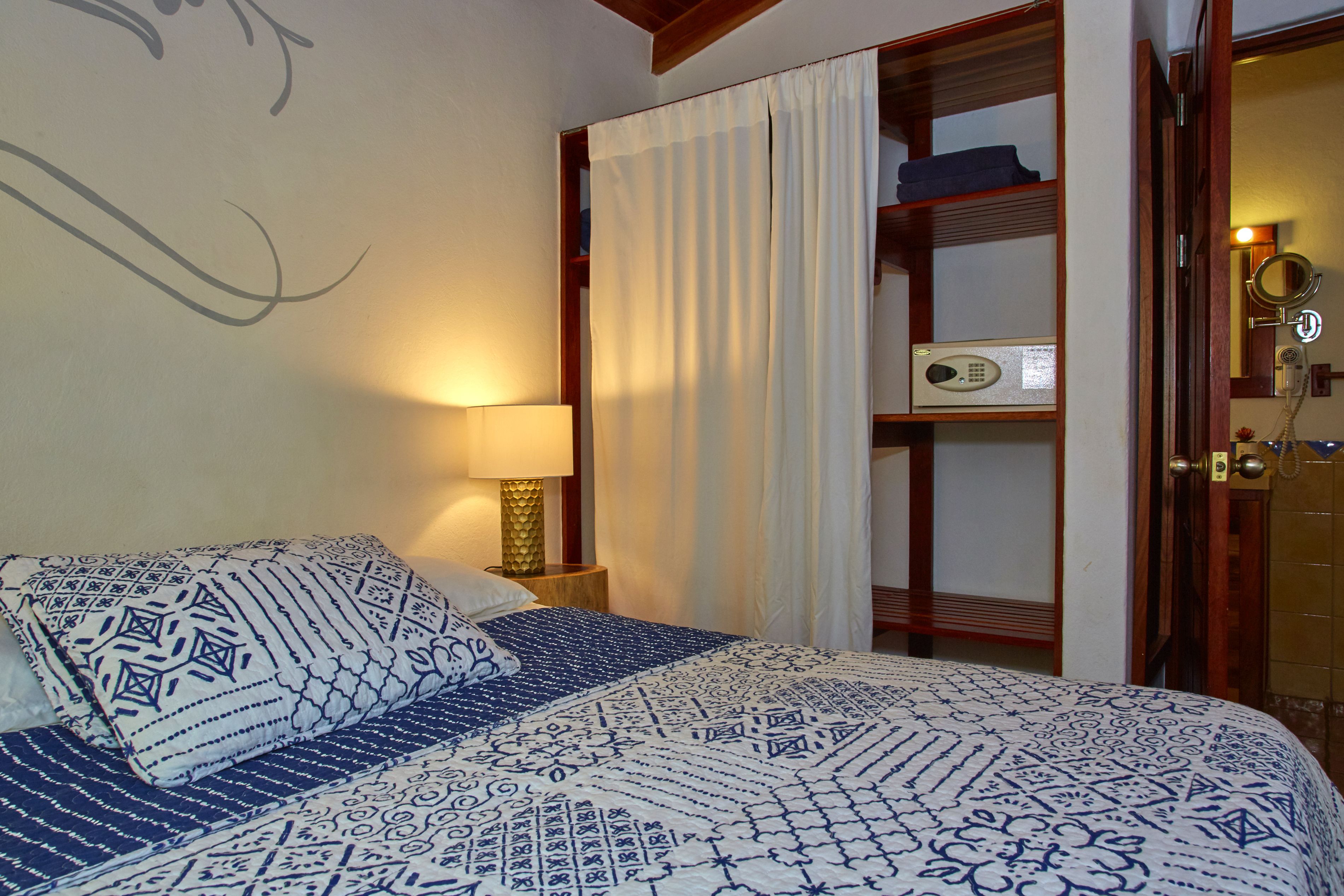 A neatly made bed with patterned bedding, a bedside lamp, a wooden nightstand, and a shelf with a radio and a telephone.