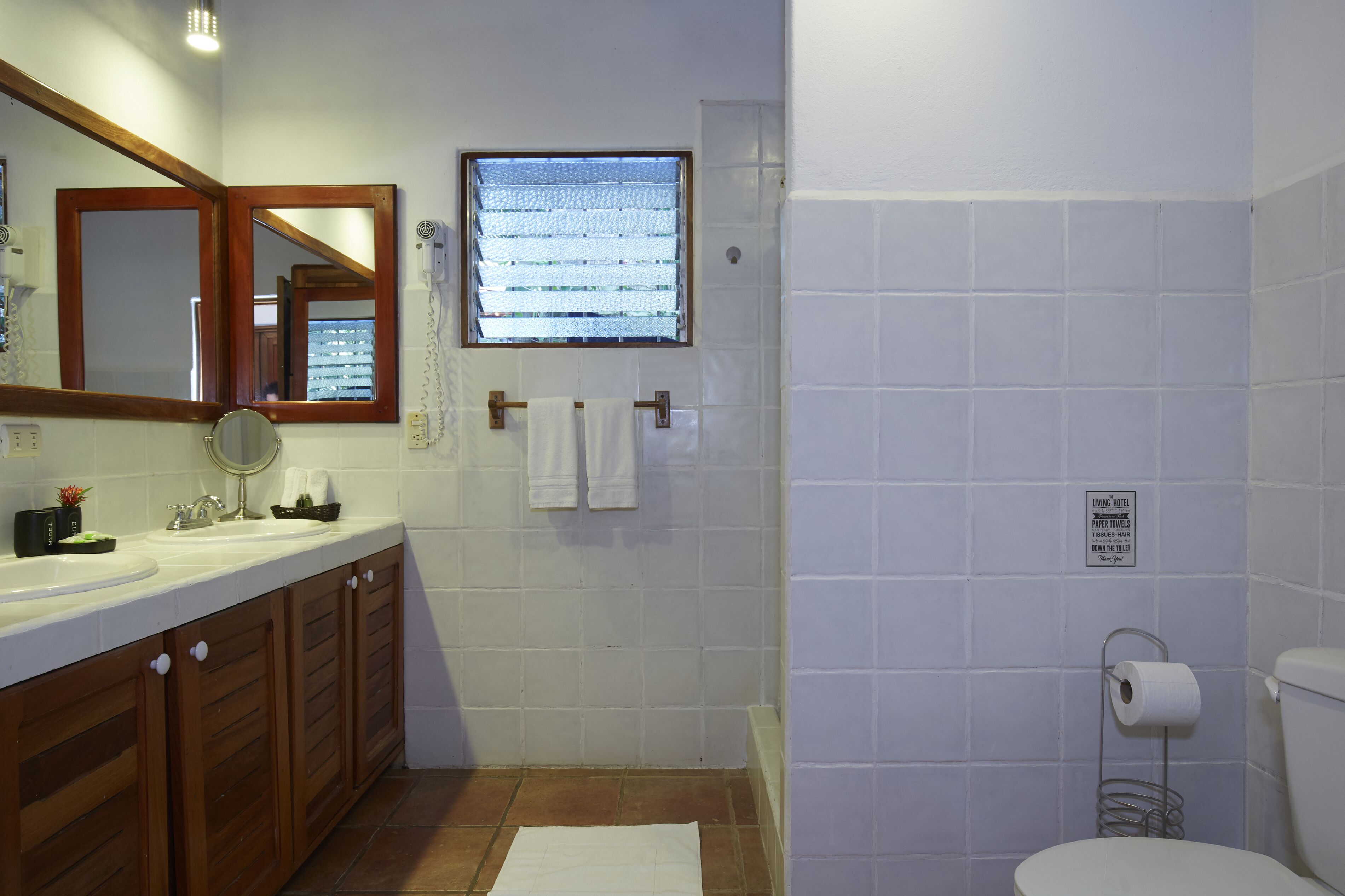Une salle de bain avec un meuble-lavabo en bois, un miroir, une fenêtre et des toilettes.