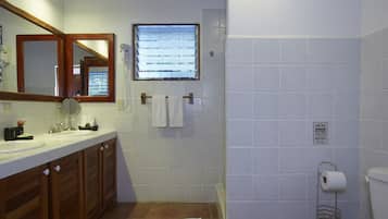 A bathroom with a wooden vanity, a mirror, a window, and a toilet.