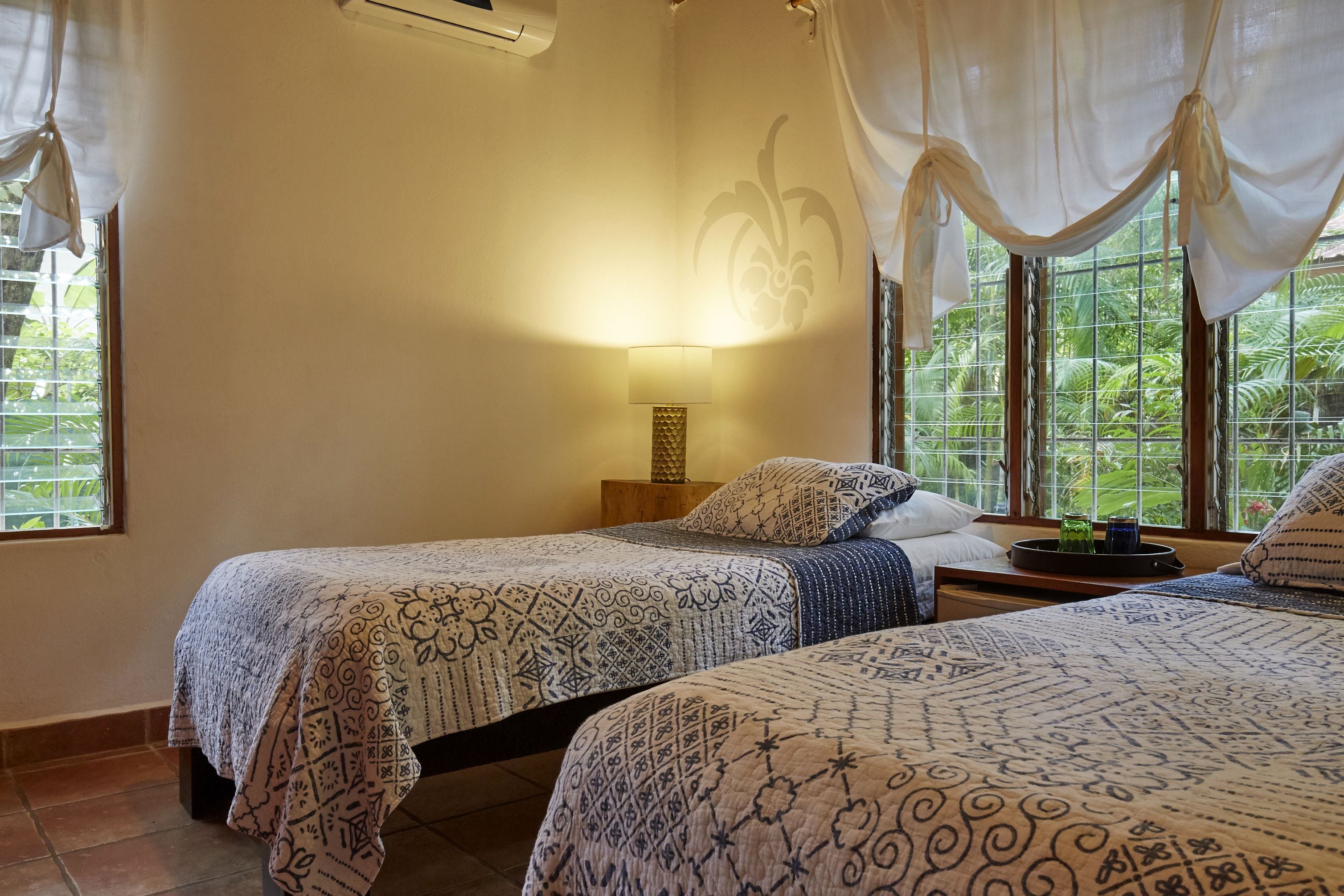Ein Zimmer mit zwei Betten, einem Nachttisch mit Lampe und Blick auf Grünanlagen durch das Fenster.