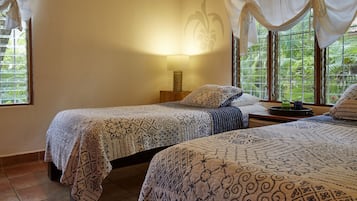 Ein Zimmer mit zwei Betten, einem Nachttisch mit Lampe und Blick auf Grünanlagen durch das Fenster.