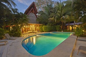 A swimming pool surrounded by lounge chairs and a building with a thatched roof.