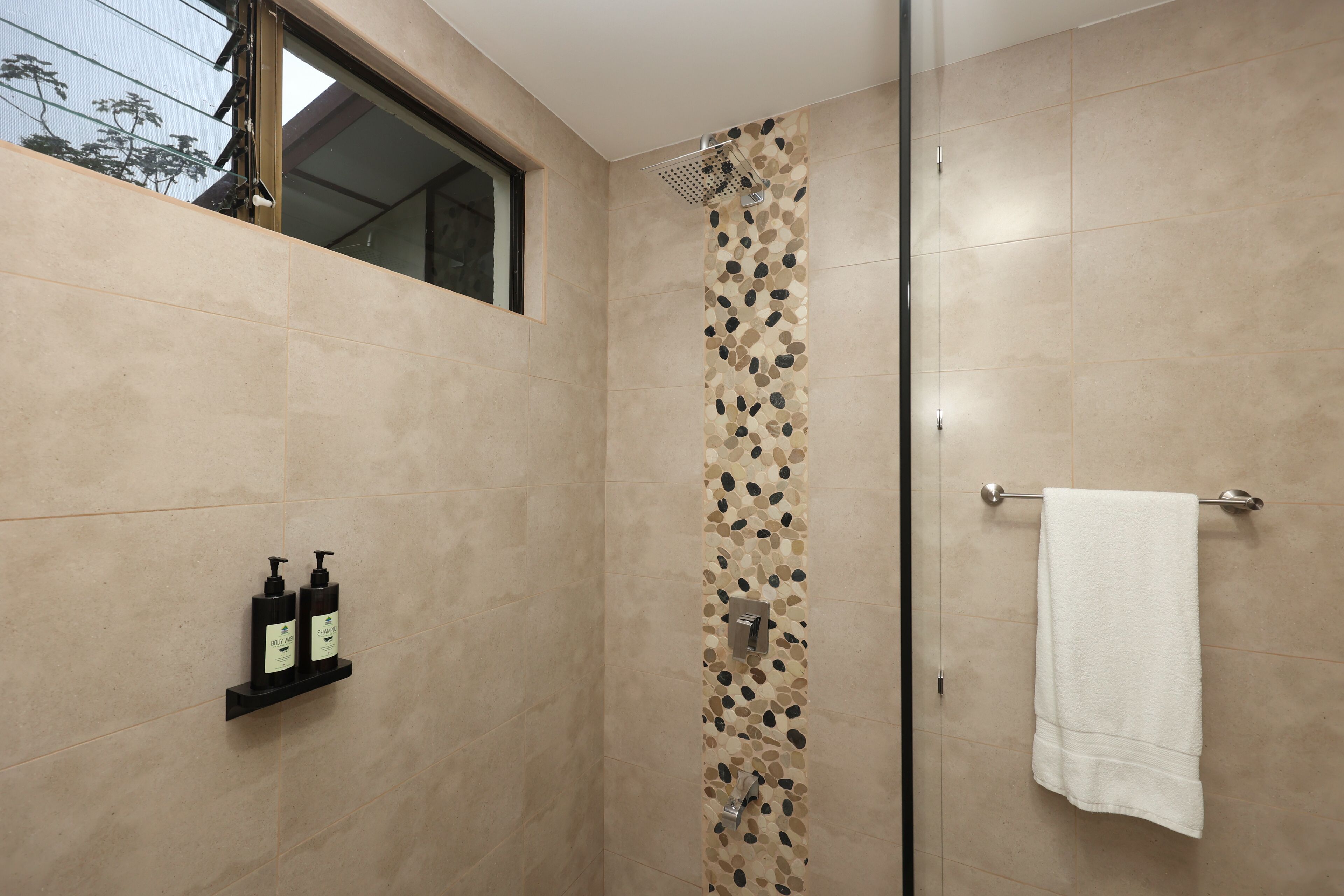Ducha moderna con pared de diseño tipo piedra, puerta de cristal y toalla blanca colgada en una barra de metal.
