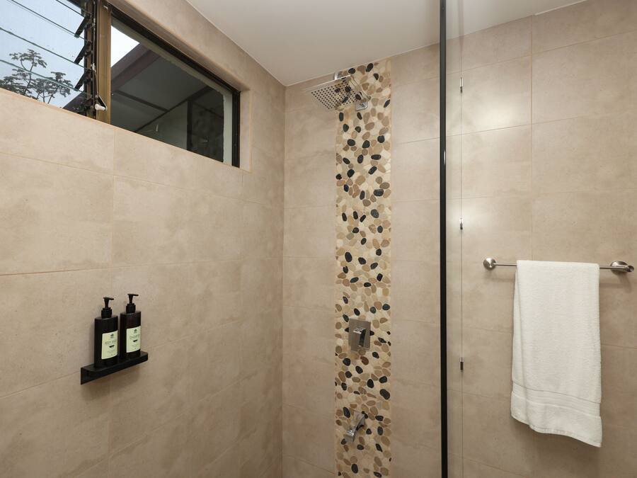 Ducha moderna con pared de diseño tipo piedra, puerta de cristal y toalla blanca colgada en una barra de metal.