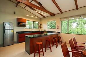 A modern kitchen with a central island, wooden stools, and a refrigerator.