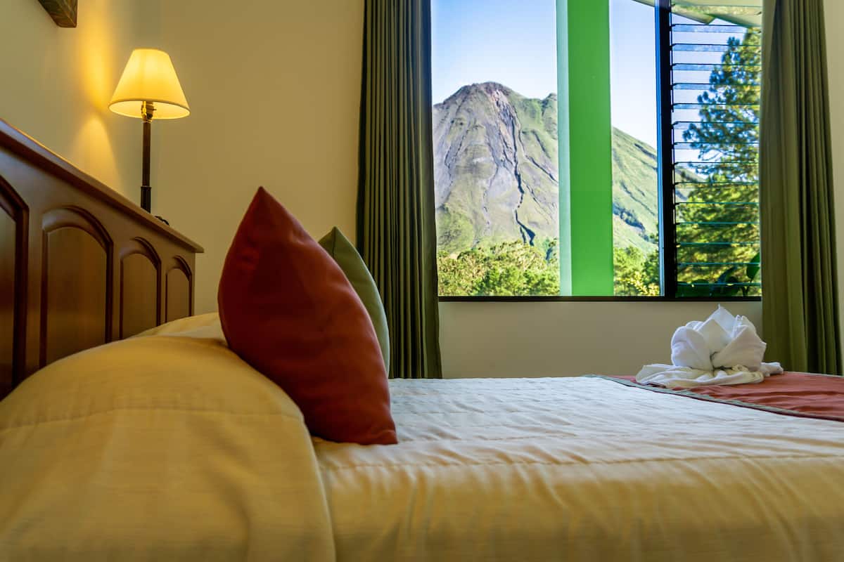 A hotel room with a bed, a lamp, a window with a mountain view, and a towel on the bed.