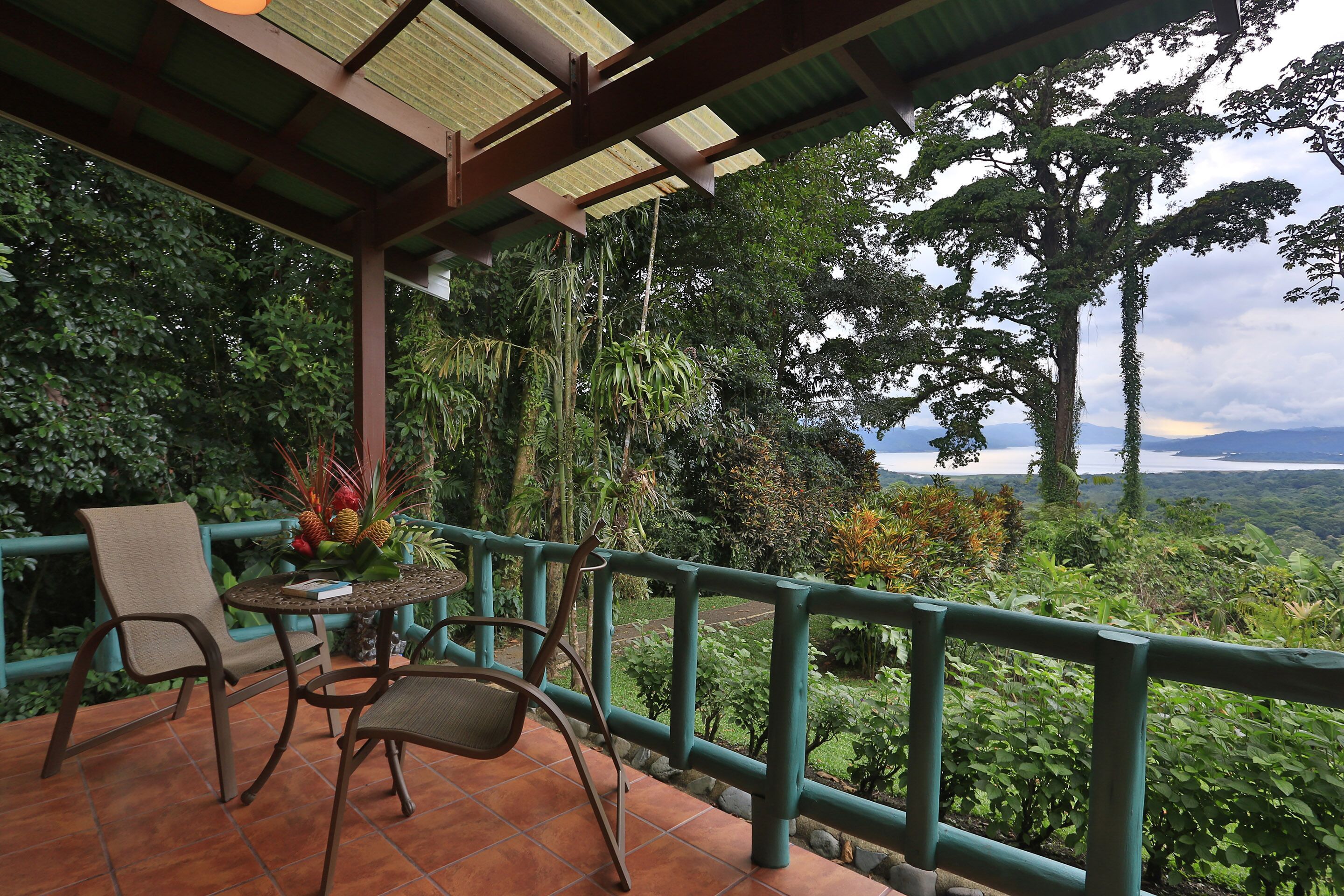A terrace with a table and chairs, surrounded by lush greenery and a view of distant mountains.