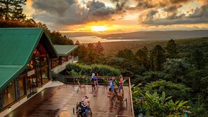 A wooden deck with a restaurant, overlooking a scenic landscape with a sunset view. - Arenal Observatory Lodge & Trails (La Fortuna)