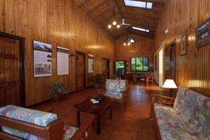 A wooden interior with a wooden ceiling, a sofa, a table, chairs, and a TV.