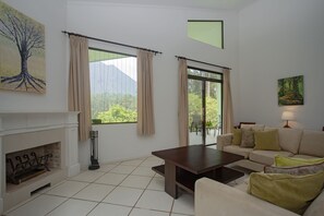 A living room with a fireplace, a sofa, a coffee table, and large windows with curtains.