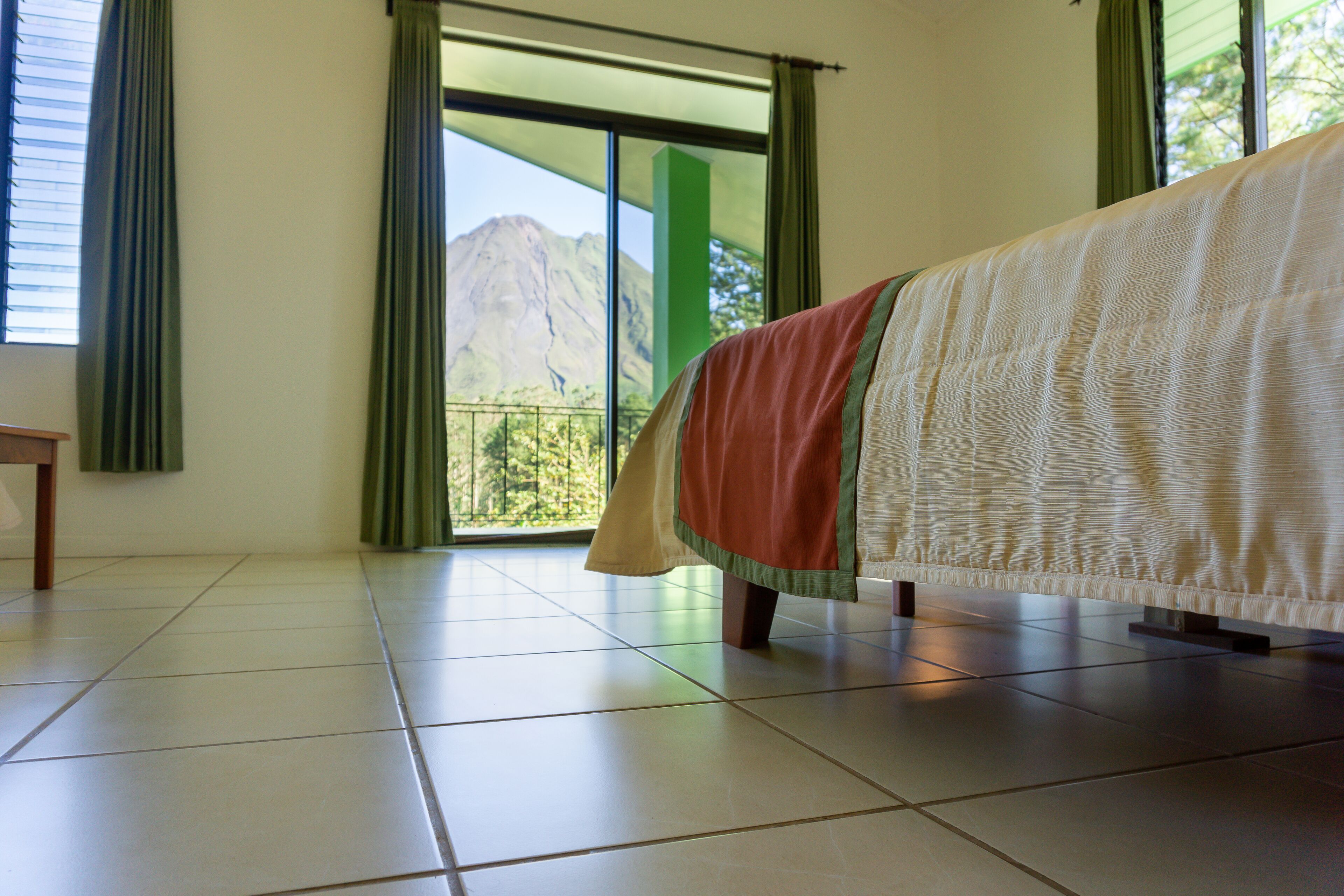 Habitación de hotel con cama, vista a la montaña a través de un ventanal grande y suelo de baldosas.