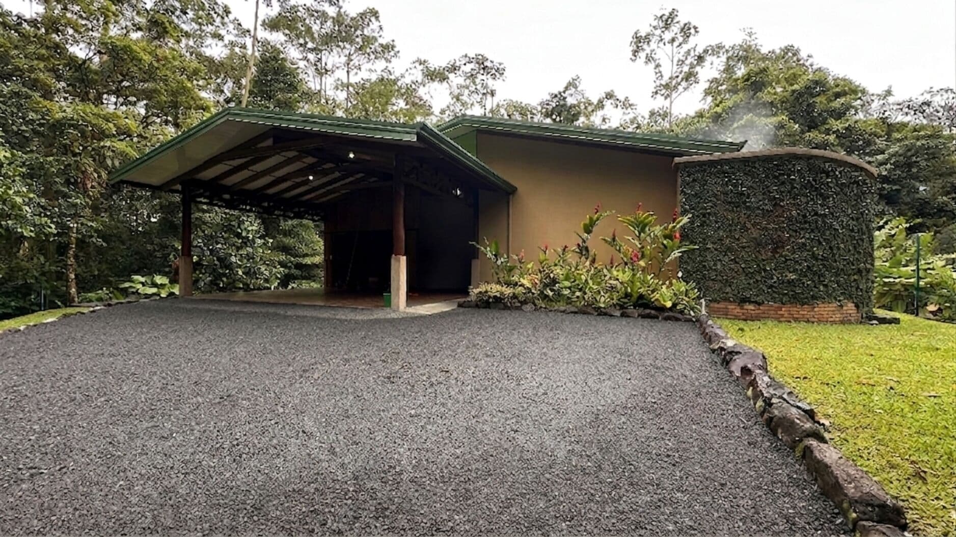 A building with a covered entrance, a gravel driveway, and a well-maintained garden.