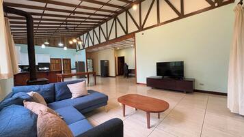 Amplia sala de estar con sofá, una mesa de centro, televisor y cocina al fondo.