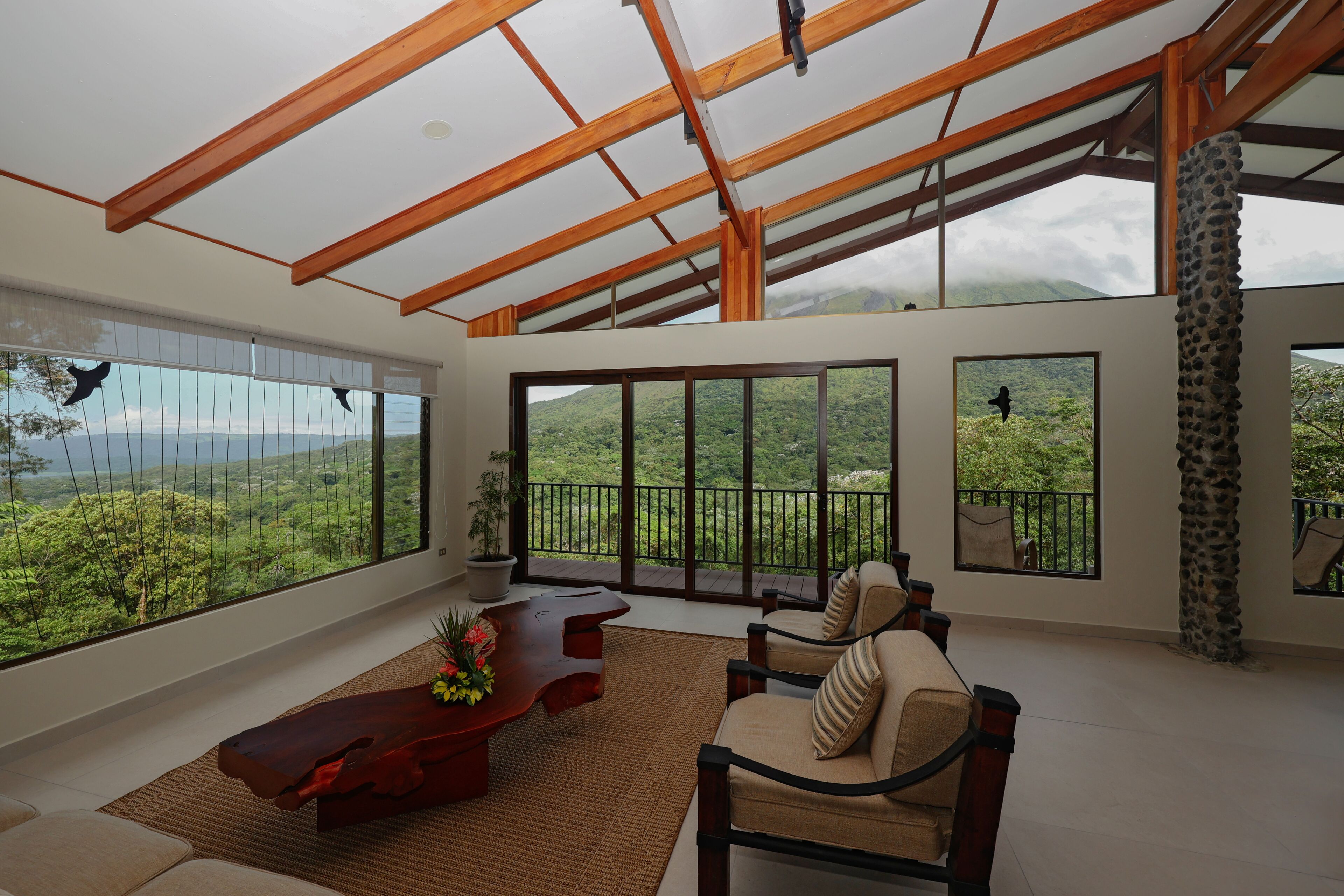 A spacious room with large windows offering a view of lush greenery and a mountainous landscape.