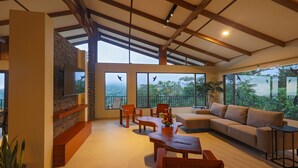 A spacious living area with a wooden ceiling, large windows, a sofa, and a coffee table. - Arenal Observatory Lodge & Trails (La Fortuna)