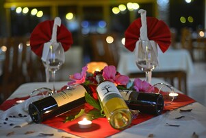 Una mesa dispuesta con botellas de vino, copas y una vela, con lazos rojos sobre el mantel.
