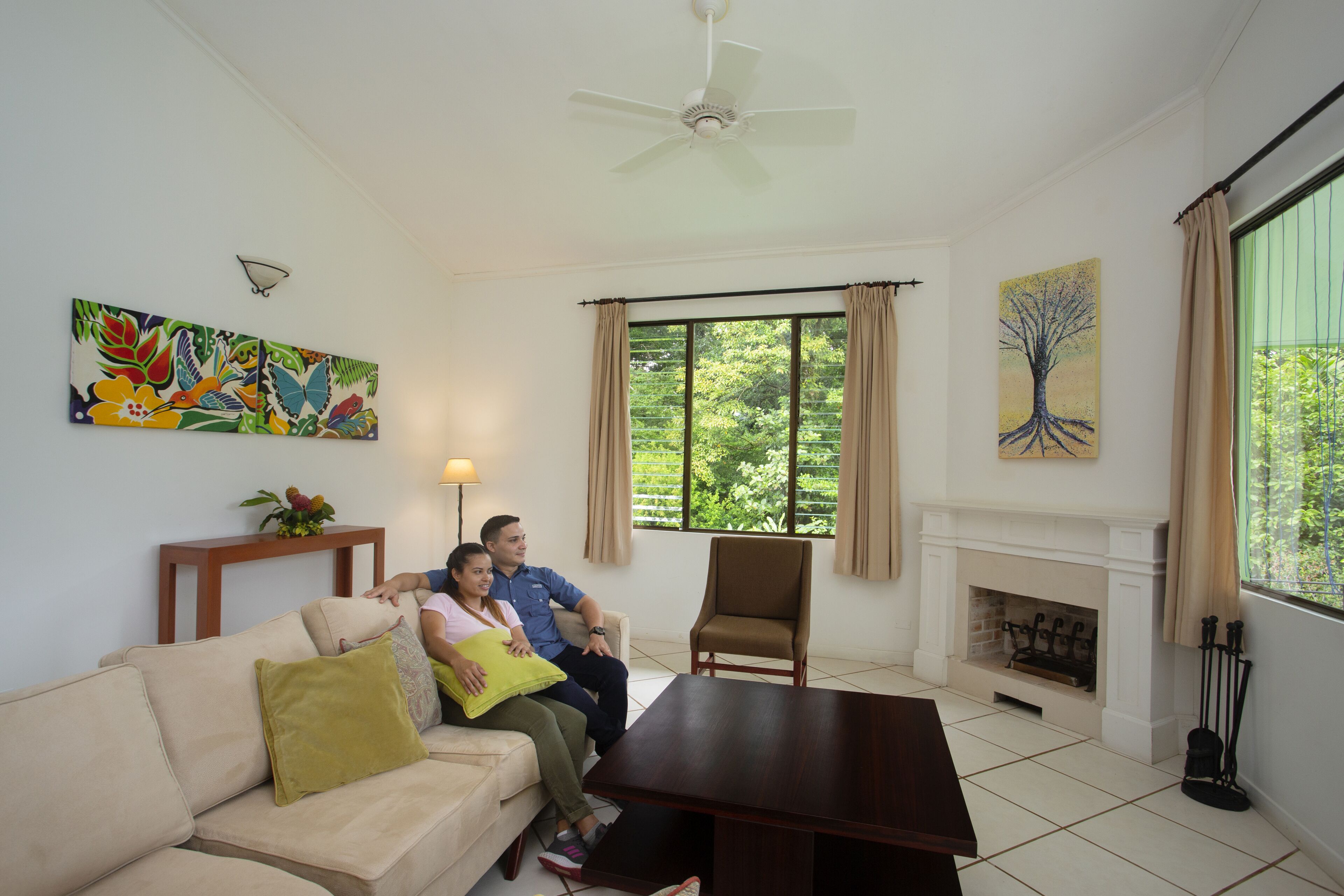 Una sala de estar con un sofá, una mesa de centro, una chimenea y un ventanal con cortinas.