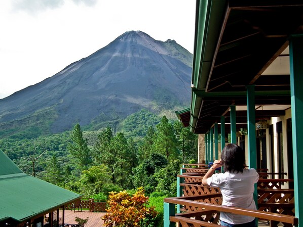 A view of a mountain from a wooden balcony with a green roof. - Arenal Observatory Lodge & Trails (La Fortuna)
