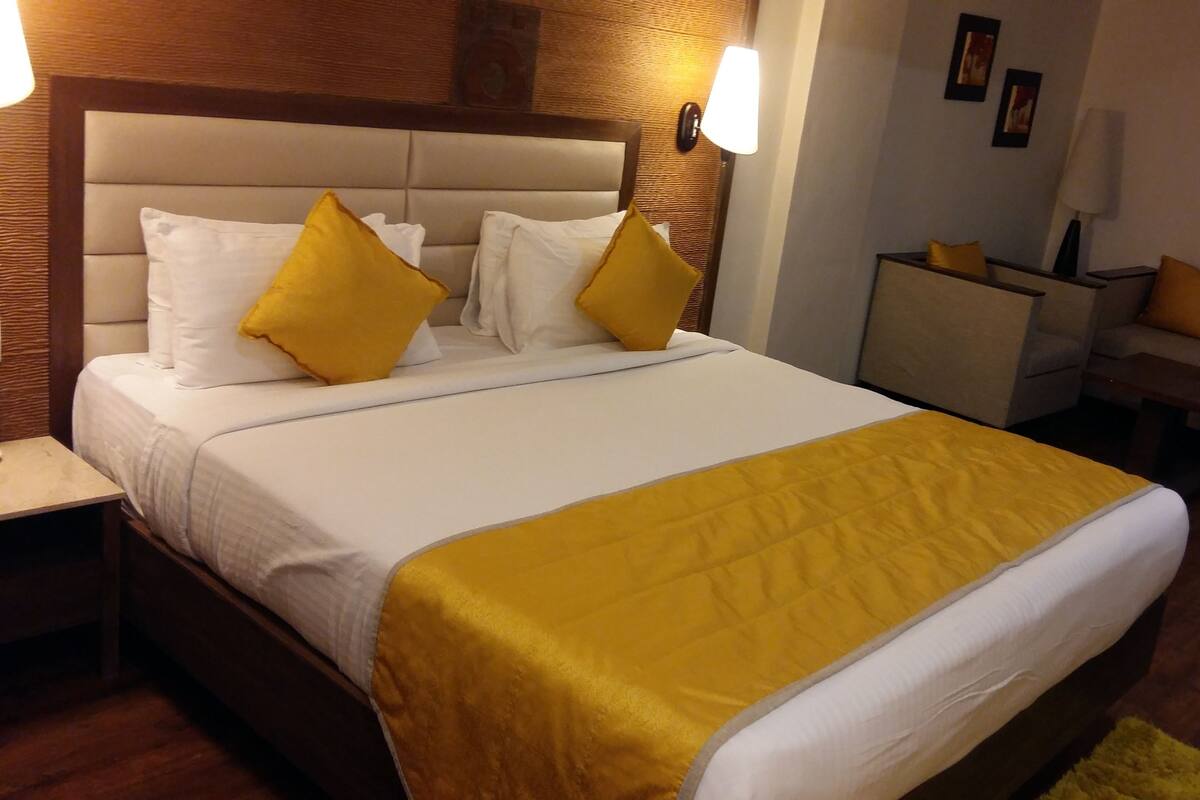 A hotel room with a large bed, a nightstand, a sofa, and a wooden headboard.