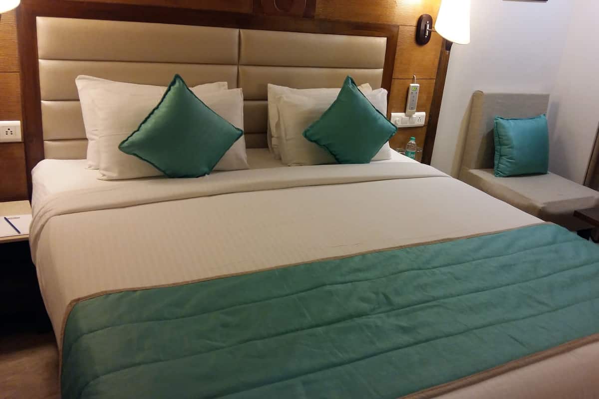 A hotel room with a large bed, two pillows, a bedside table, a nightstand, and a lamp.