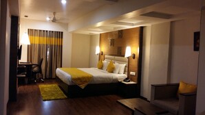 Una habitación de hotel con cama, lámparas de noche, un escritorio con silla, una mesita y un sofá.