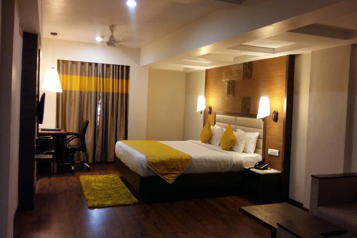 A hotel room with a bed, bedside lamps, a desk with a chair, a small table, and a sofa.