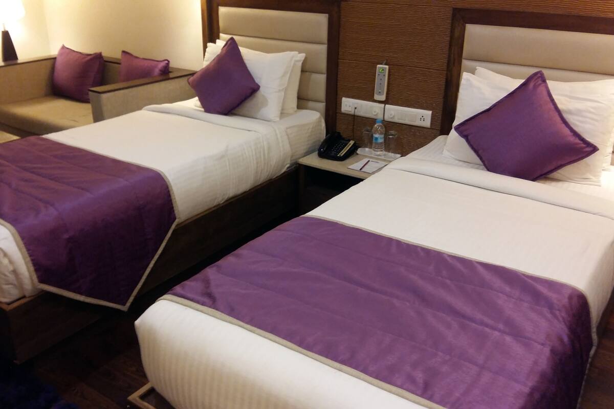 A hotel room with two beds, each with a purple bedspread and white pillows. There is a nightstand with a phone and a bottle of water.