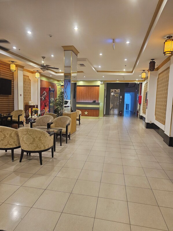 A hotel lobby with a reception desk, seating area with chairs, and a tiled floor.
