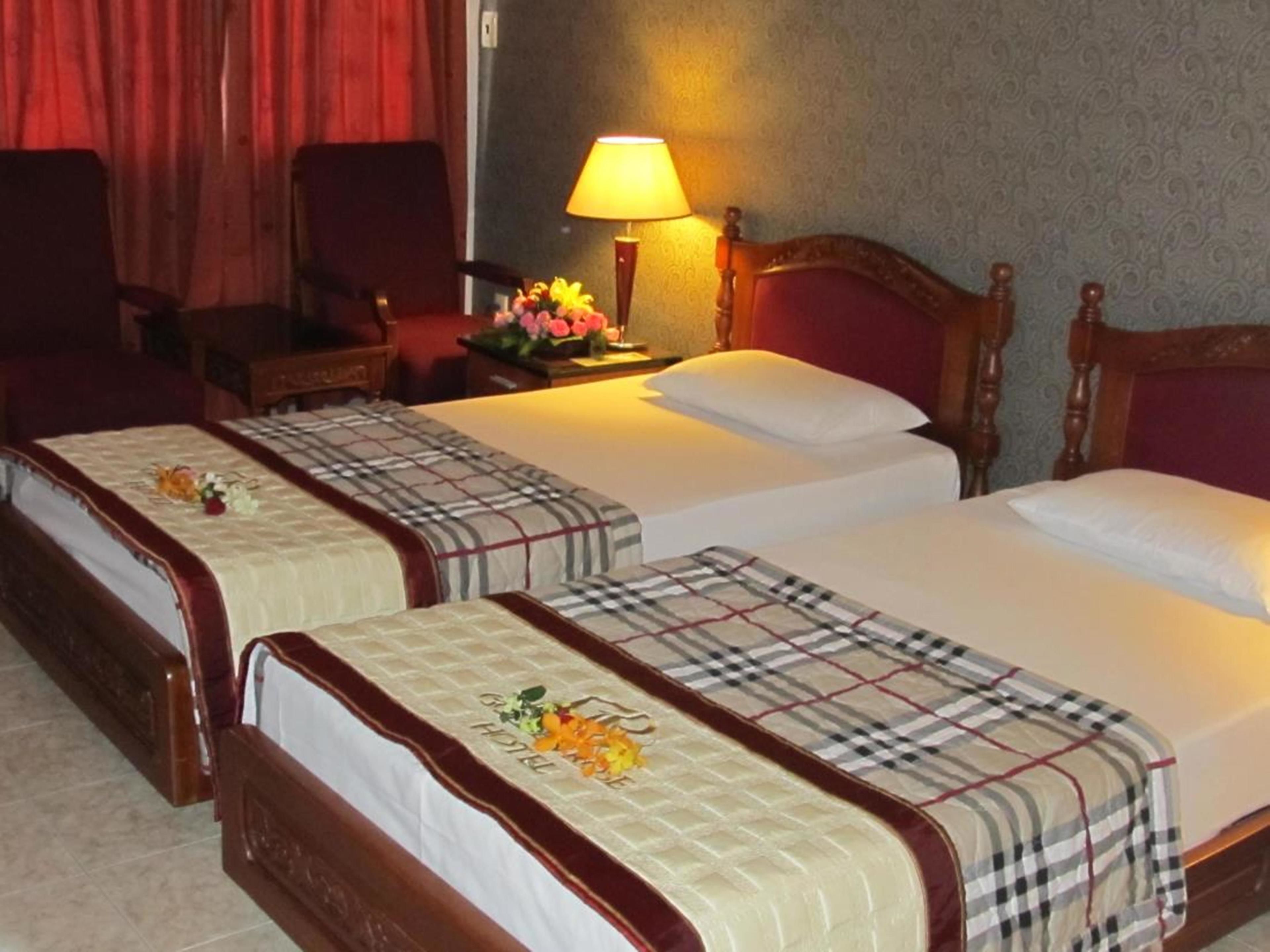 Habitación de hotel con dos camas, cada una con una colcha escocesa y un arreglo floral en la mesita de noche.