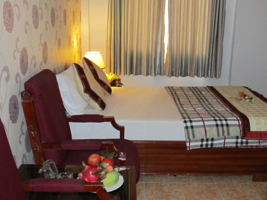 A bedroom with a bed, a chair, a table with fruit, and curtains.