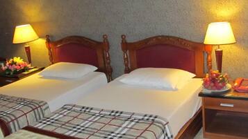 Habitación de hotel con dos camas, cada una con cabecero de madera y ropa de cama blanca. Hay dos mesitas de noche con lámparas y un frutero en una de ellas.