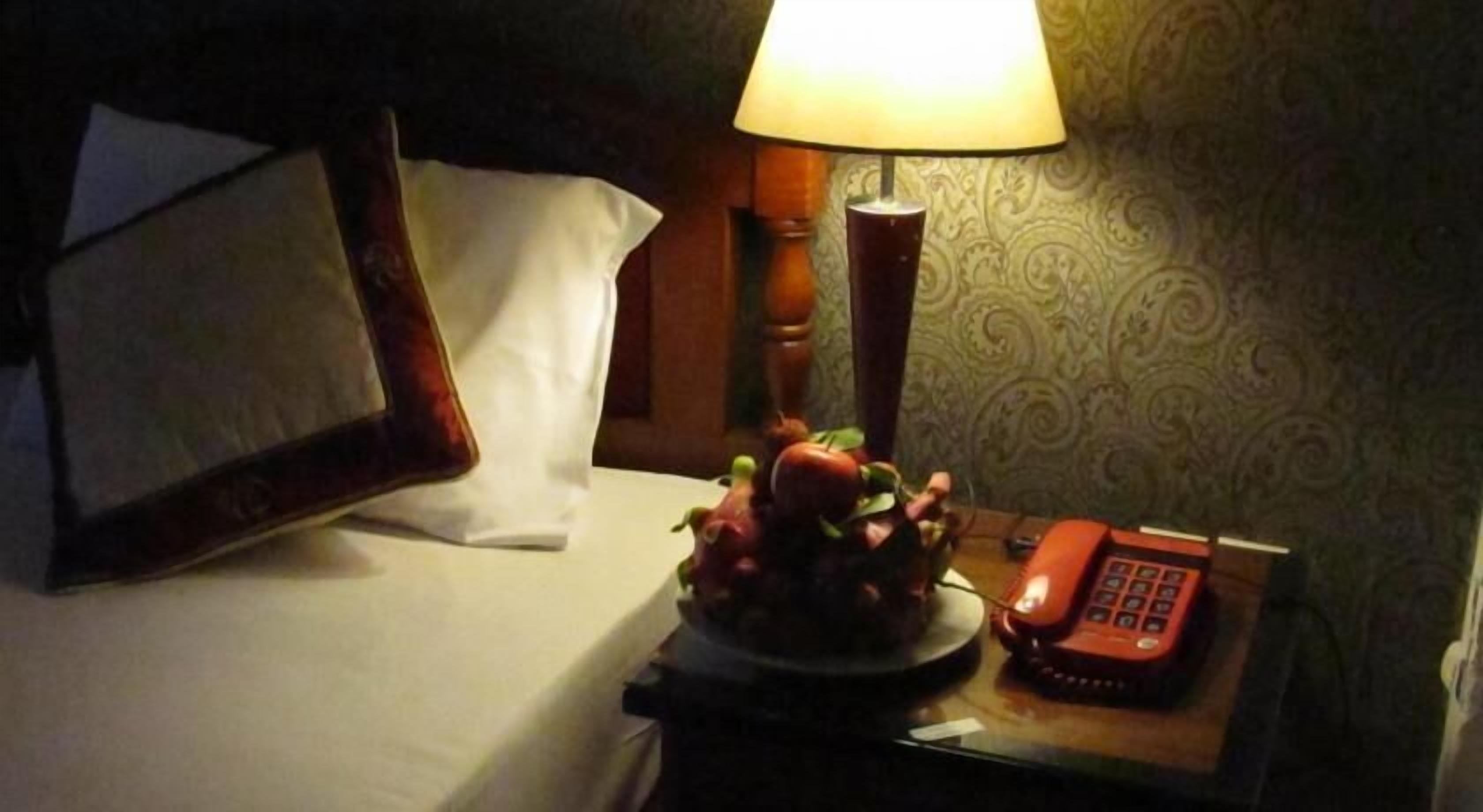 Een hotelkamer met een bed, een bedlamp, een telefoon en een decoratieve fruitschaal.