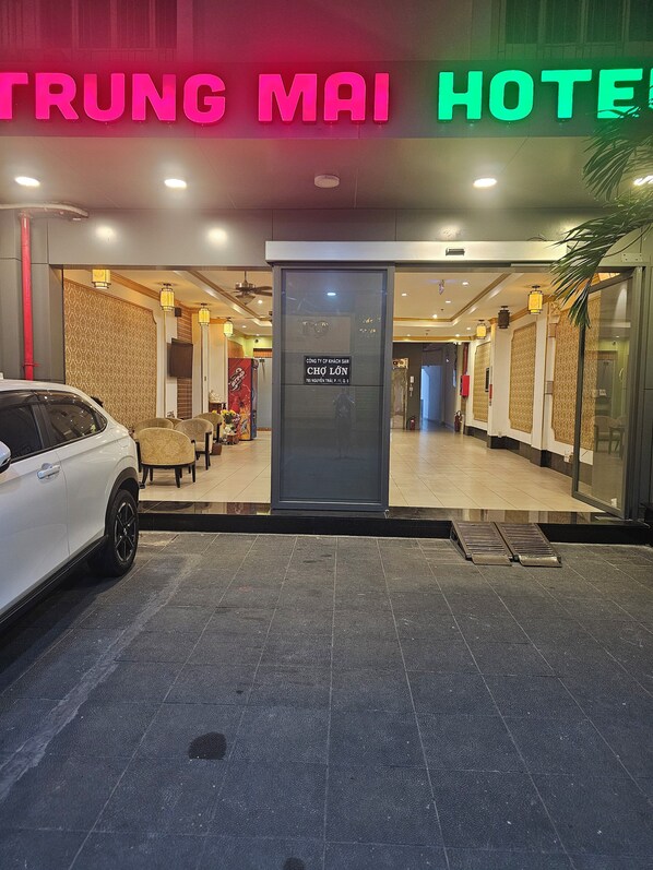 Entrada de un hotel con un letrero de neón, un mostrador de recepción y un coche estacionado afuera.