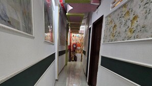 Un couloir dont le sol est recouvert de carreaux, les murs sont peints en vert et en blanc, et le plafond est orné de panneaux verts et roses.
