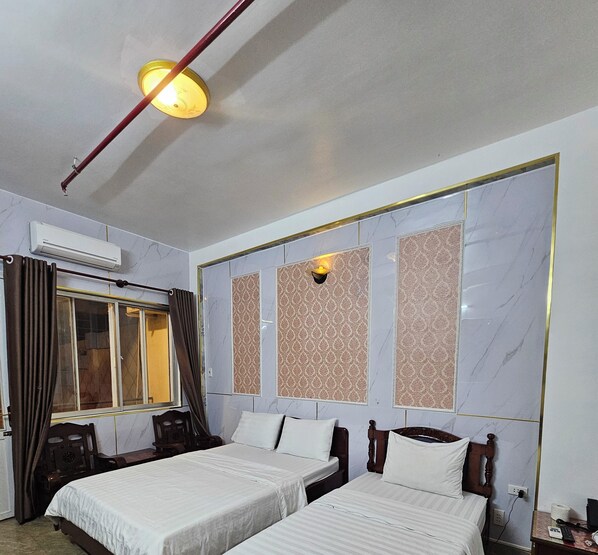 Une chambre d’hôtel avec deux lits, une fenêtre avec des rideaux, un appareil de climatisation et un luminaire fixé au mur.