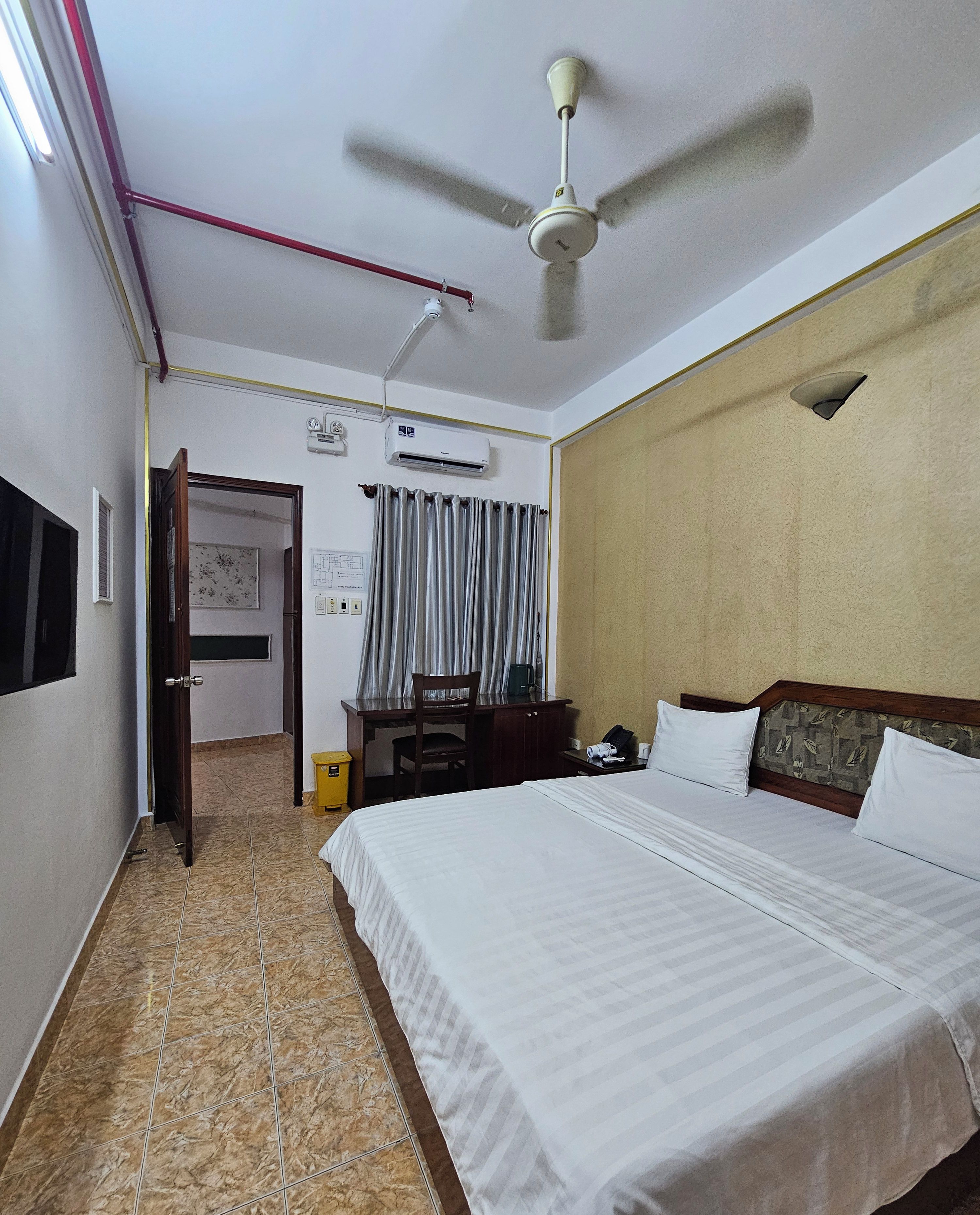 Une chambre d’hôtel équipée d’un lit, d’un bureau, d’une chaise, d’un climatiseur et d’un ventilateur de plafond.