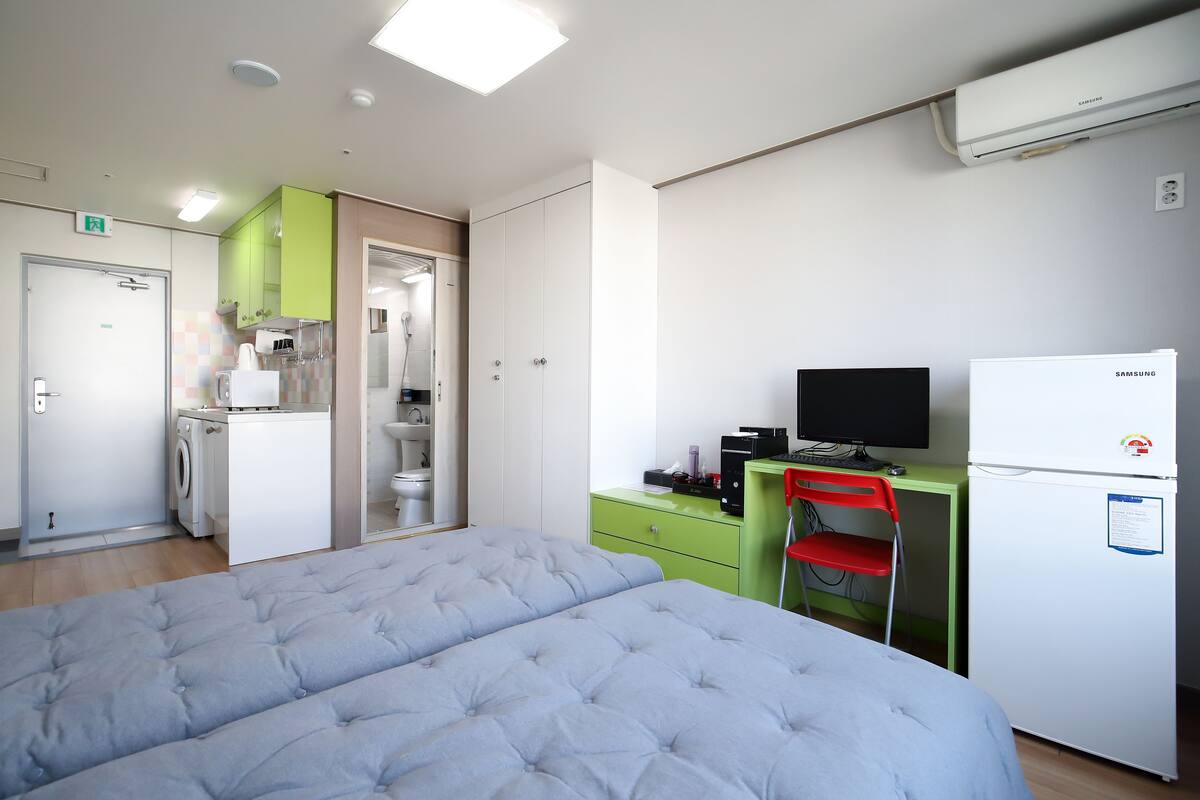A bedroom with a bed, a desk with a computer, a television, and a refrigerator.