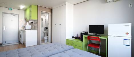 A bedroom with a bed, a desk with a computer, a television, and a refrigerator.