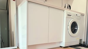 A compact kitchen with a built-in washer and dryer, wooden flooring, and white cabinetry. - SB Guest House (Suwon)