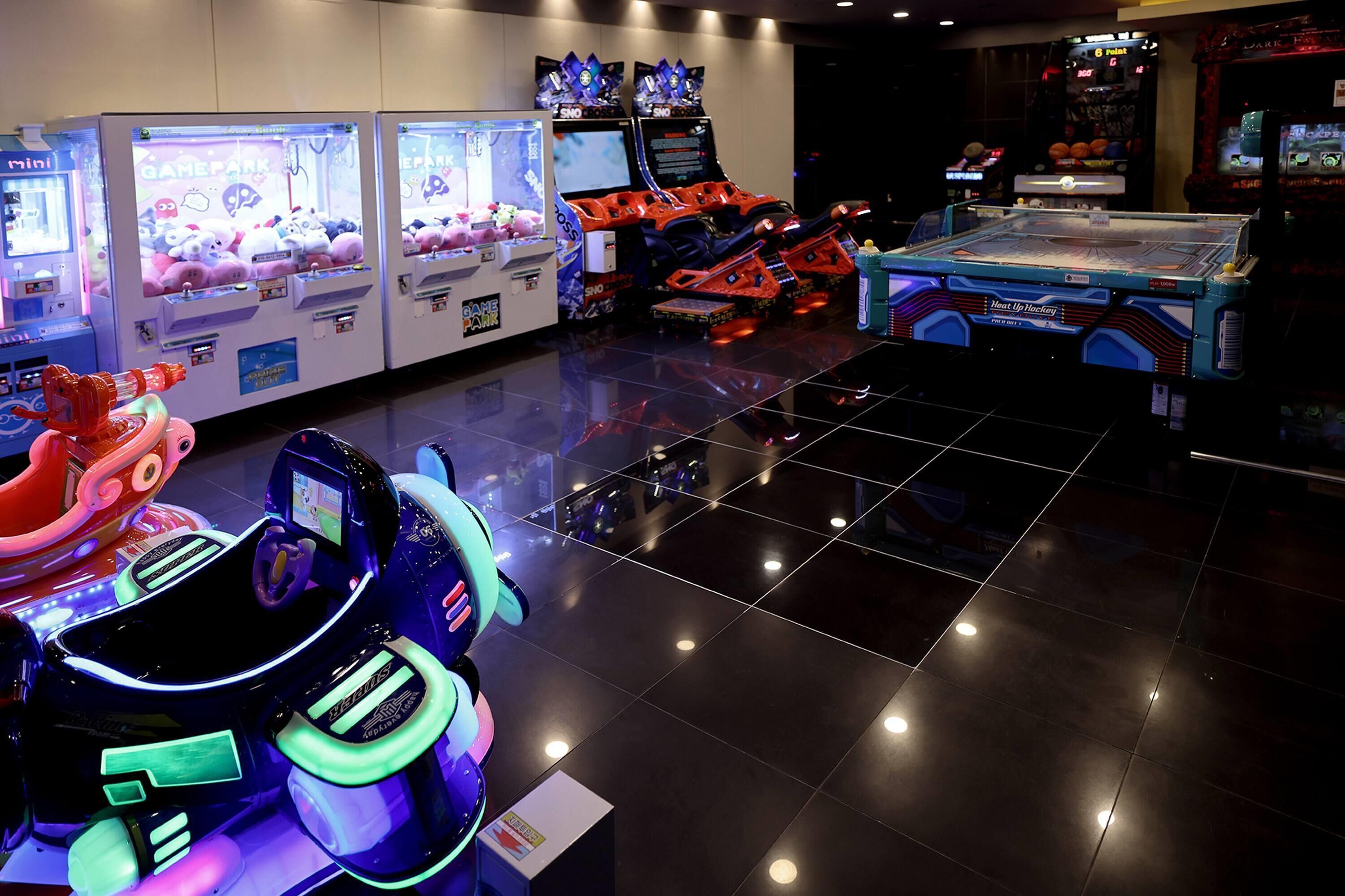 A variety of arcade games and rides, including claw machines and bumper cars, in a brightly lit indoor space.