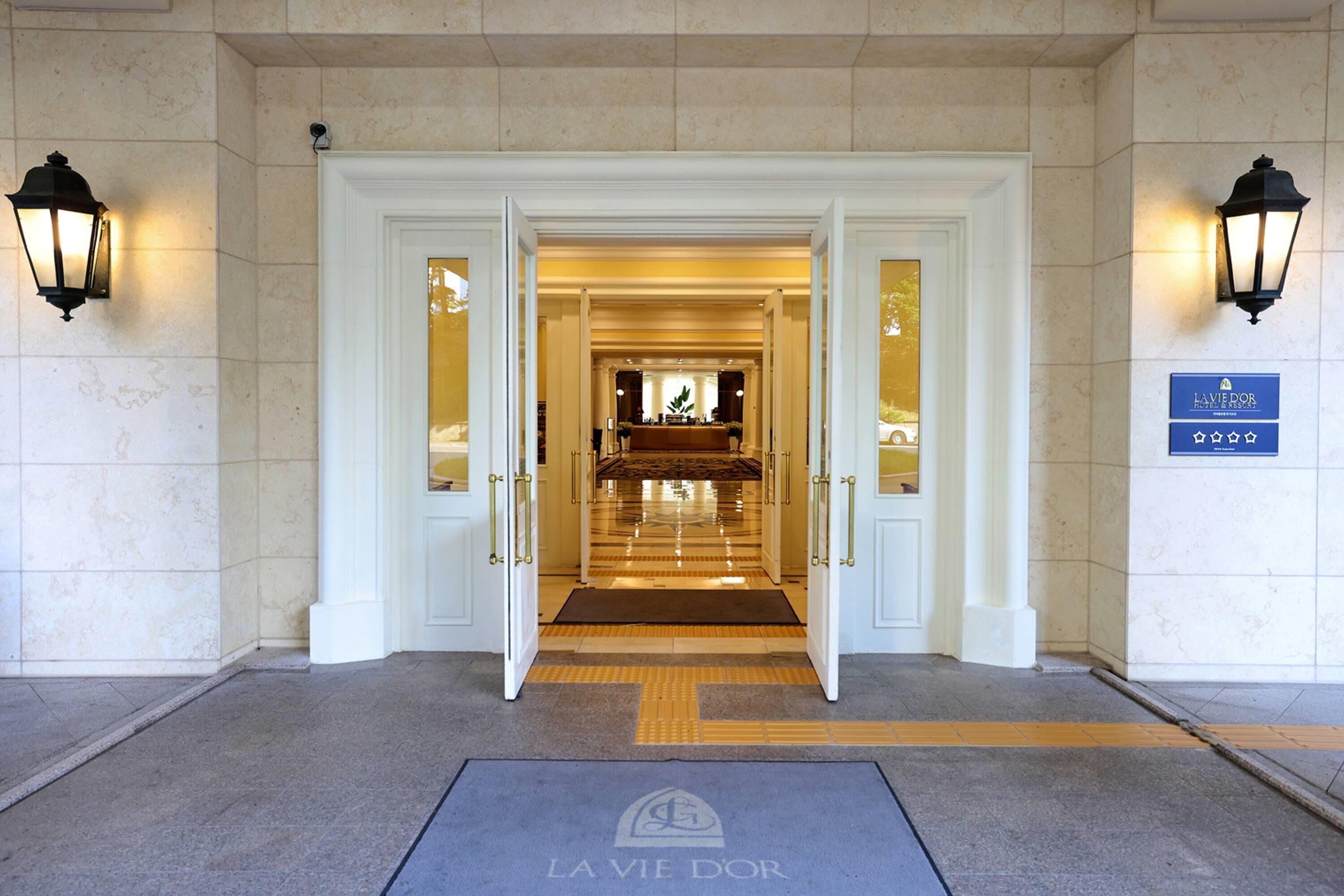 Entrada de hotel con piso de mármol, puertas dobles y un mostrador de recepción al fondo.