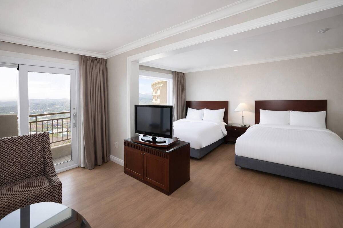 A hotel room with a bed, a TV on a wooden cabinet, a desk, and a chair.