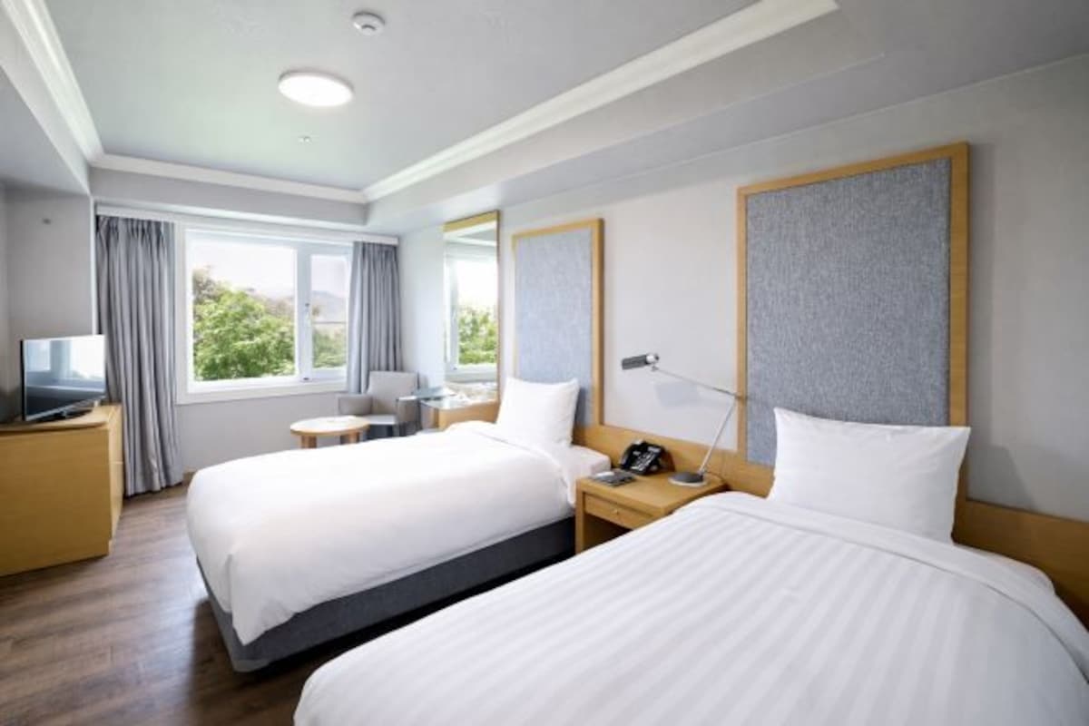 A hotel room with two beds, a TV, a desk, and a chair.