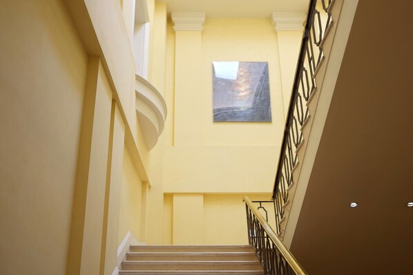 A staircase with a handrail, a painting on the wall, and a yellow wall.
