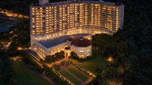 A large, multi-story hotel with a curved facade, surrounded by well-maintained gardens and a sports field. - La Vie Dor Hotel and Resort, Trademark Collection by Wyndham (Hwaseong)